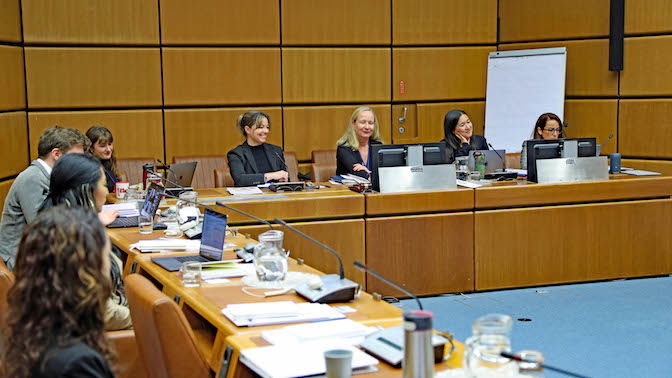 A panel with five women. On the left side, a man and two women sitting behind tables.
