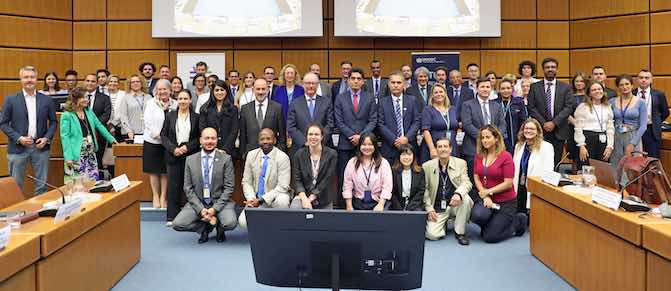 A group photo taken in a meeting room arranged in three rows. Behind the participants of a meeting, two roll up banners: on the left side, the roll up banner of Stakeholder Engagement for UNTOC (SE4U) and on the right side, the roll up banner of the UNTOC Review Mechanism.