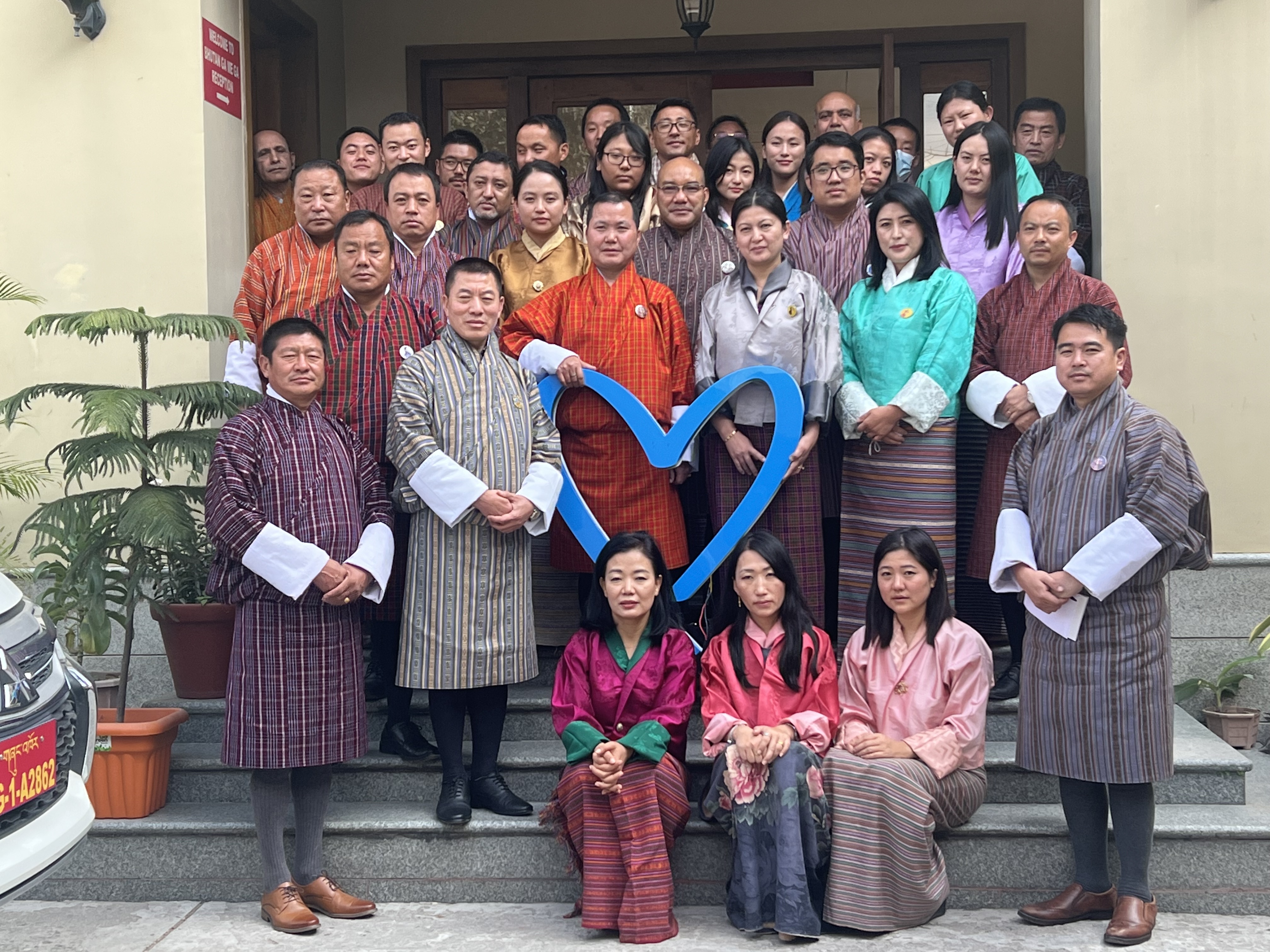 Group photo taken outside a building. A man in the group is holding a heart-shaped symbol. 