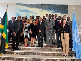 A group photo taken inside a building. On the left side, the flag of Jamaica. On the right side, the flag of the United Nations. 