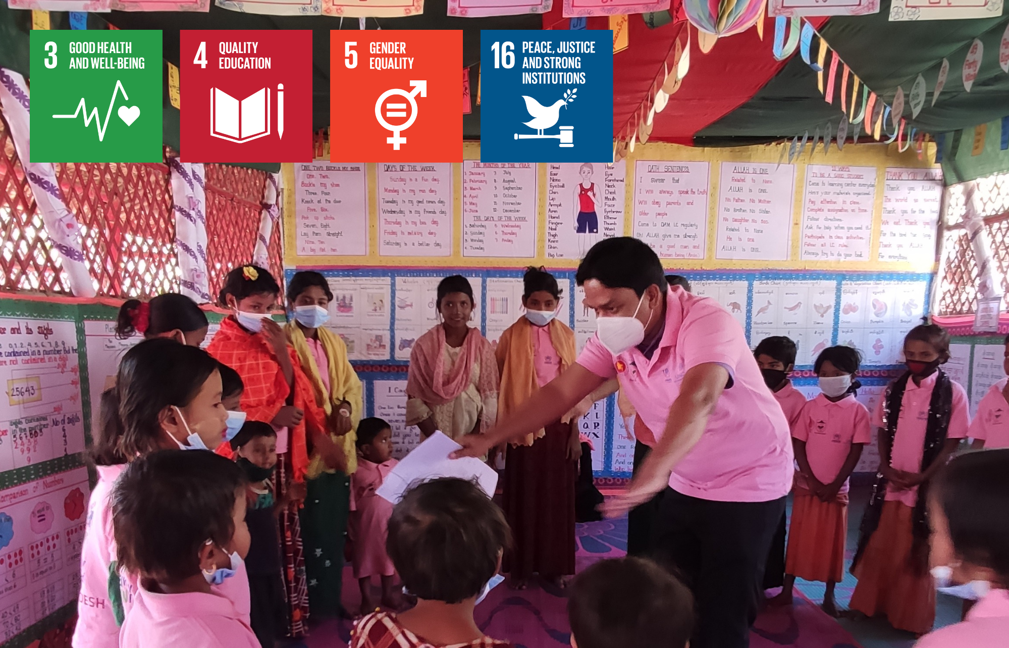 Children in a classroom setting wearing pink shirts being led through a training by an instructor. The SDG logos for SDG 3, SDG 4, SDG 5 and SDG 16 are also featured in the image. 