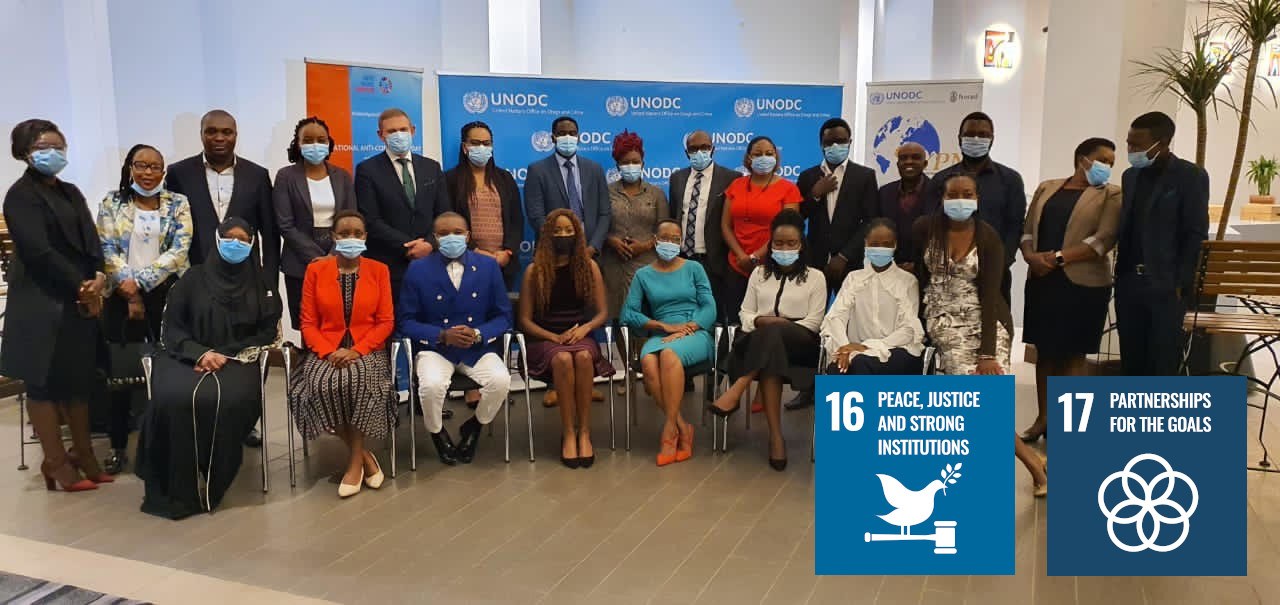 Group of people with UNODC in the background with the SDG 16 and SDG 17 logos featured. 