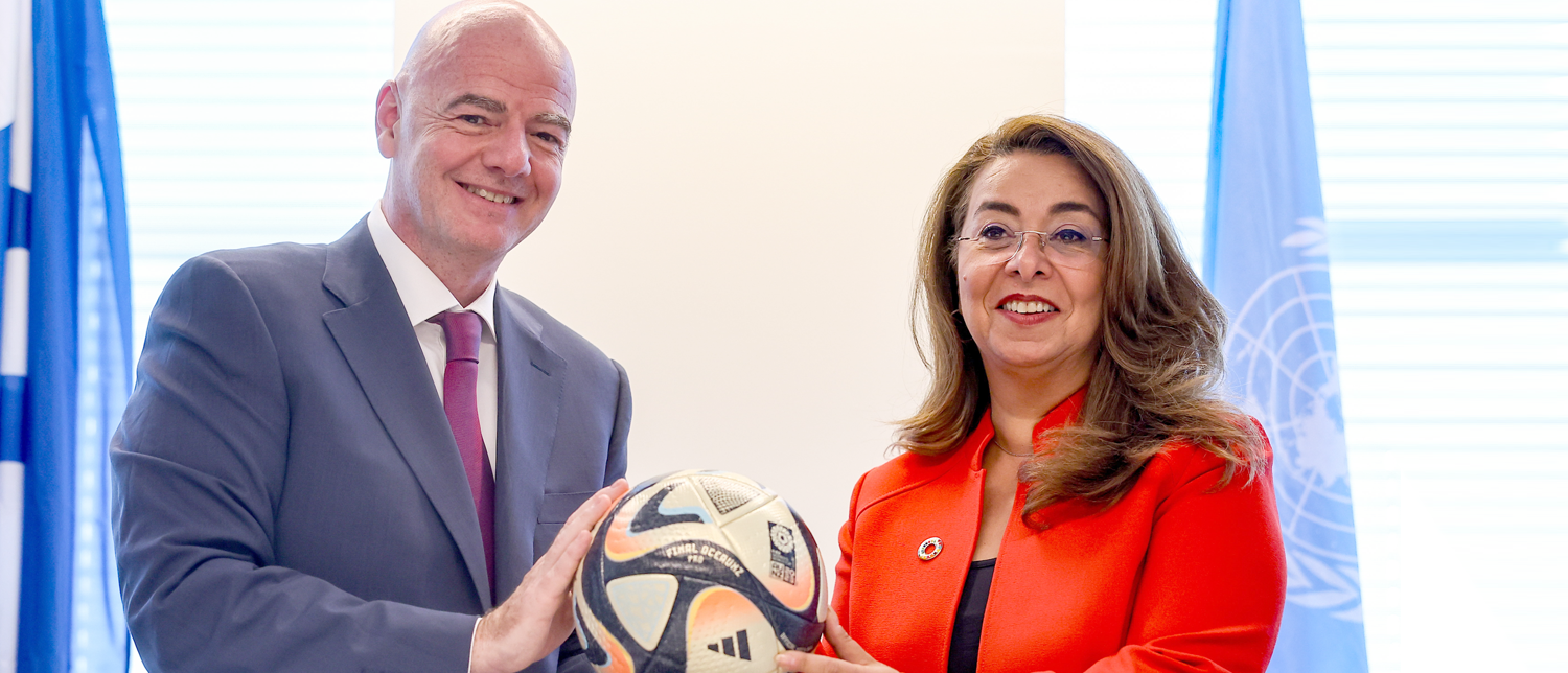 The FIFA President and UNODC Executive Director stand next to each other holding a soccer ball. 