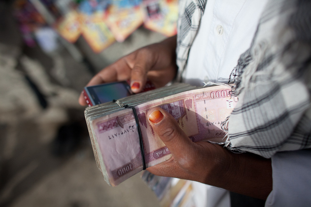 Hands holding wads of Afghan banknotes.