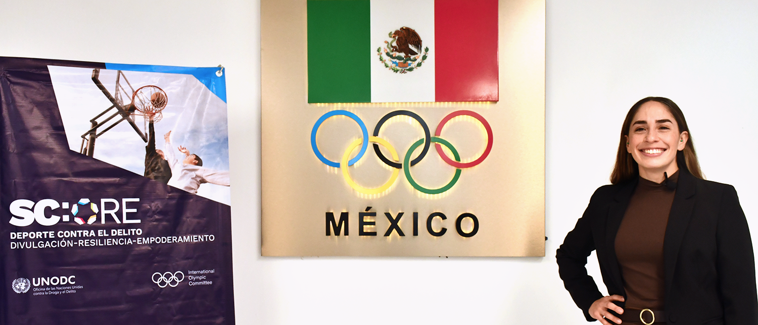 Woman next to roll-up banner, Mexican flag and the logo of the Olympic games.