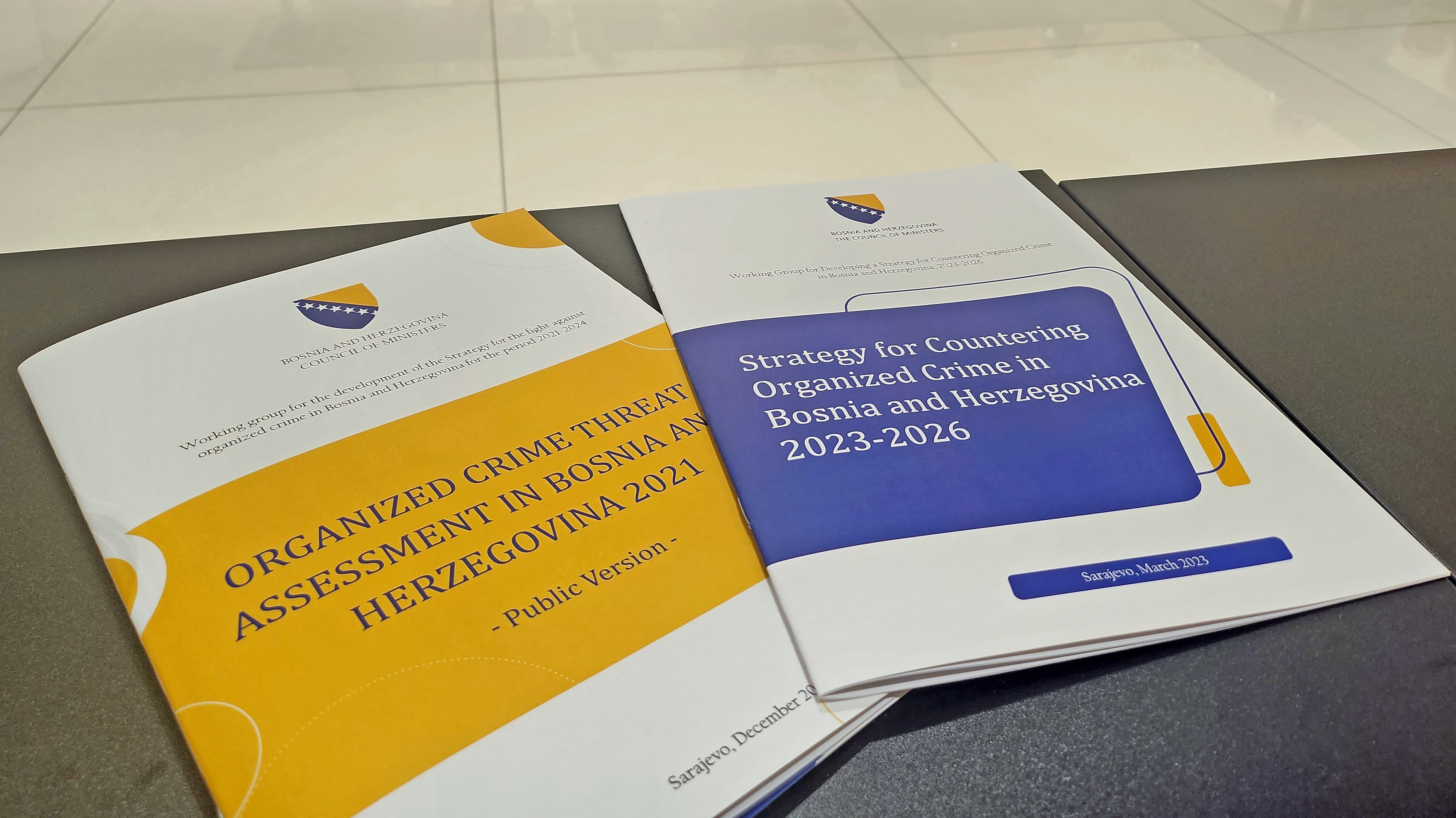 On a table, two publications: "Organized Crime Threat Assessment in Bosnia and Herzegovina 2021 - Public Version" and "Strategy for Countering Organized Crime in Bosnia and Herzegovina 2023-2026". 